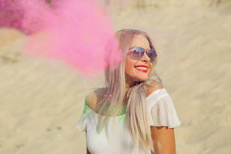 Happy blonde woman in glasses playing with pink dry paint Holi a. Happy blonde girl in glasses playing with pink dry paint Holi at the desert royalty free stock photography